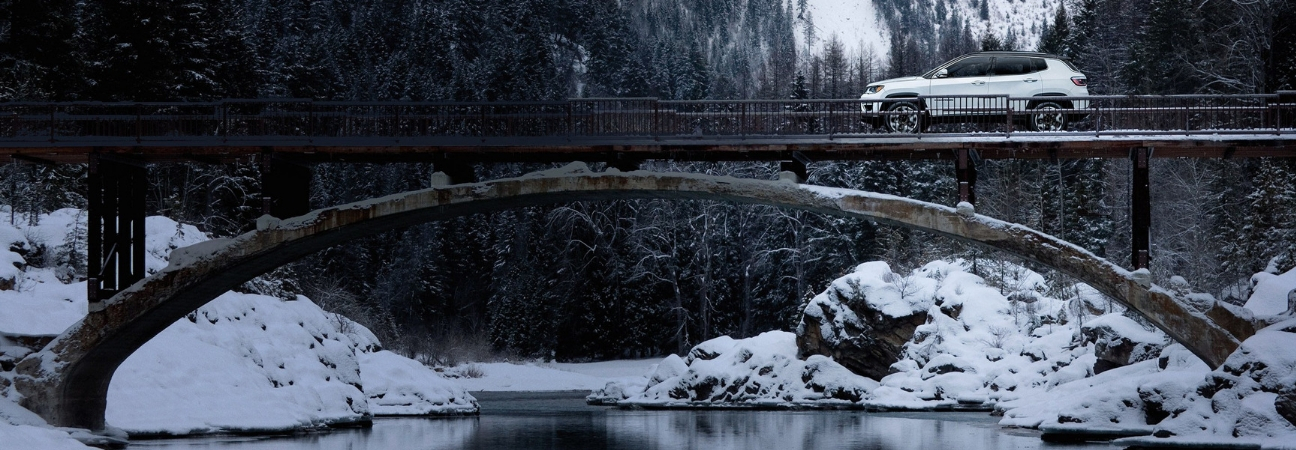 White 2018 Jeep Compass traveling over snowy bridge